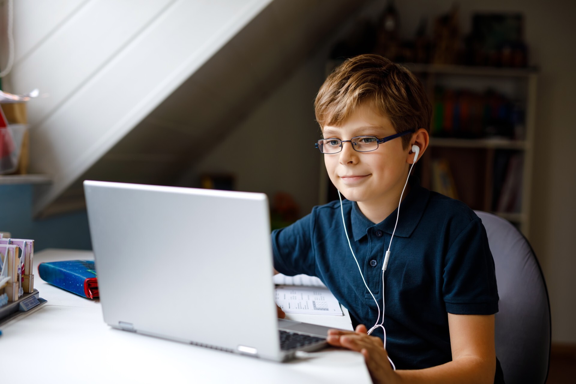 A young boy in a blue shirt with headphones in types on his computer, looking focused